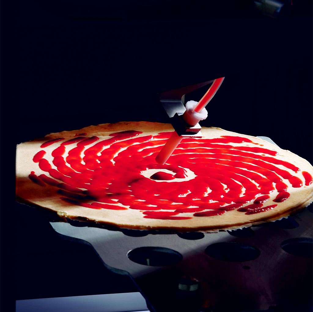 Tomato sauce being applied to a fresh pizza base inside a vending machine