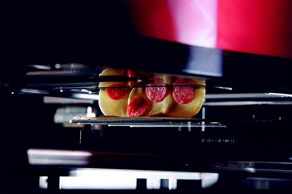 Cheese and selected toppings being added automatically to a fresh pizza